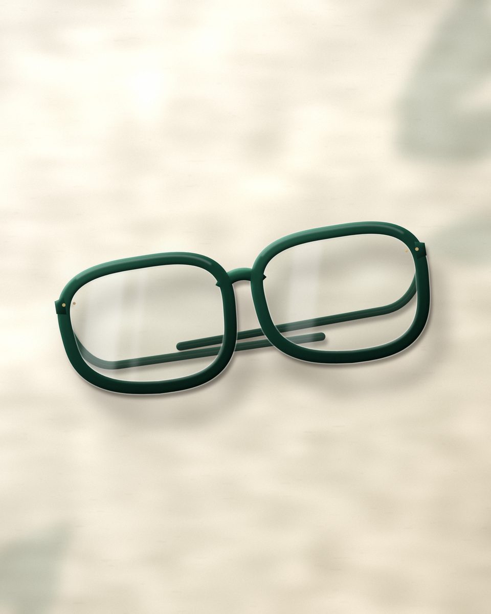 Deep green acetate eyeglasses resting on warm ivory stone in soft window light